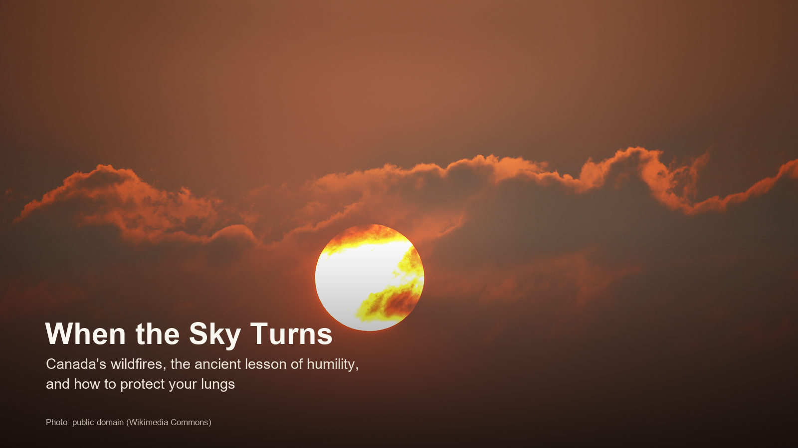 The sun glowing dim orange through thick wildfire haze